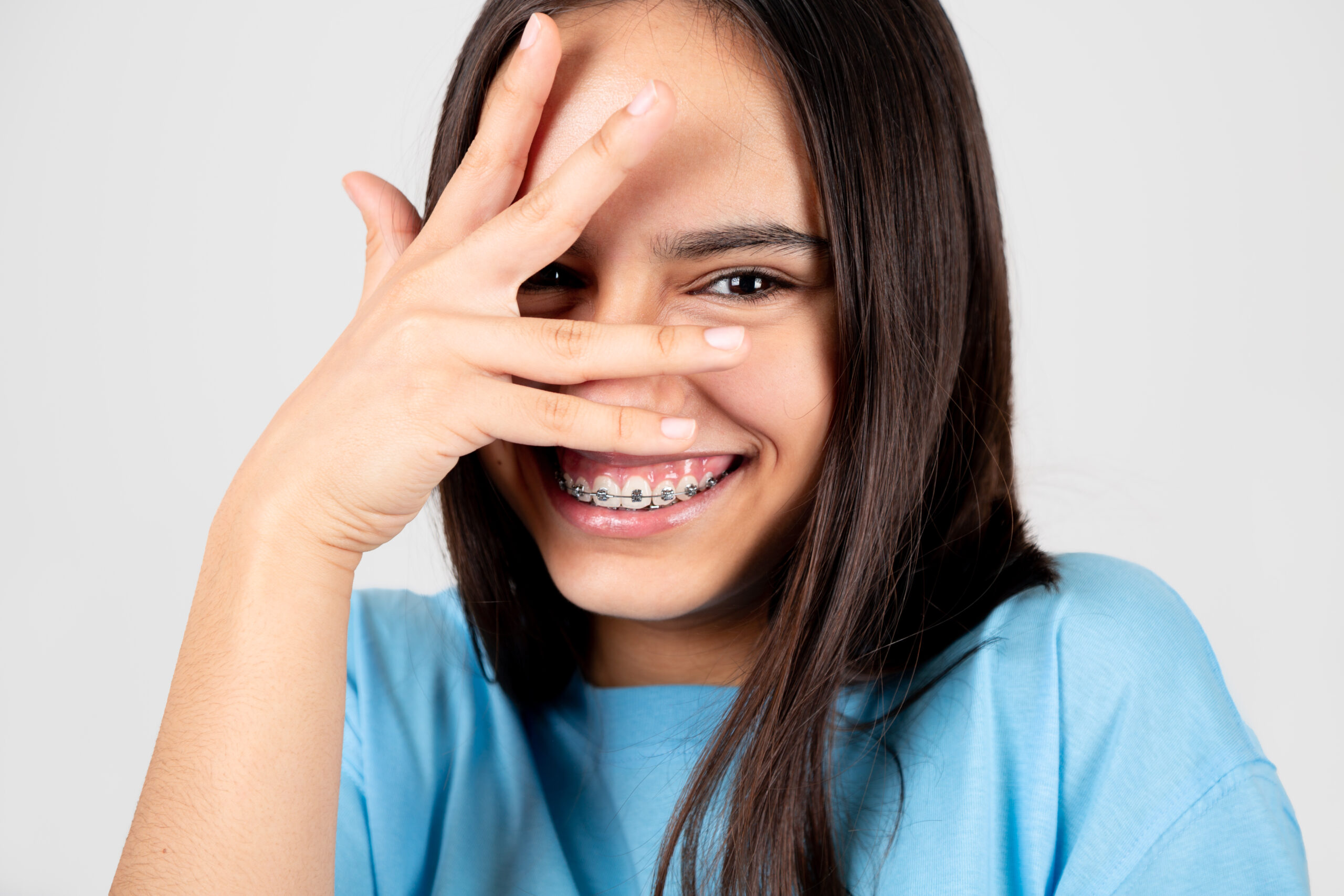 Ashamed and funny teen girl with braces covering face with hand. Isolated on white